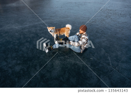 Be ready, preparing for the ride. Man with Akita Inu dog is on the ice with skates in winter Be ready, preparing for the ride. Man with Akita Inu dog is on the ice with skates in winter 135643143