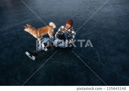 Be ready, preparing for the ride. Man with Akita Inu dog is on the ice with skates in winter 135643148