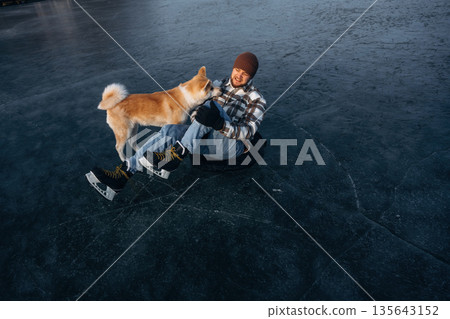 View from the top, lying down. Man with Akita Inu dog is on the ice with skates in winter View from the top, lying down. Man with Akita Inu dog is on the ice with skates in winter 135643152