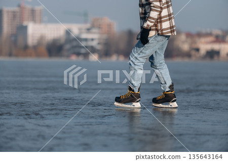 Daytime leisure activity. Close up view of man that is on ice with skates in winter Daytime leisure activity. Close up view of man that is on ice with skates in winter 135643164