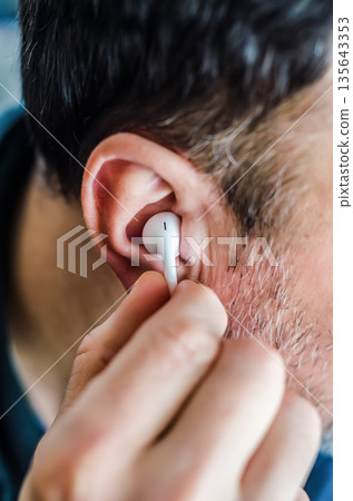 Tuning In: Close-Up of a Man Placing an Earbud in His Ear. 135643353