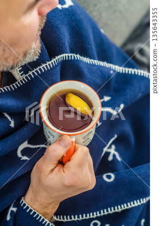 Cozy Comfort: Man Wrapped in a Blanket with Hot Tea. Cozy Comfort: Man Wrapped in a Blanket with Hot Tea. 135643355