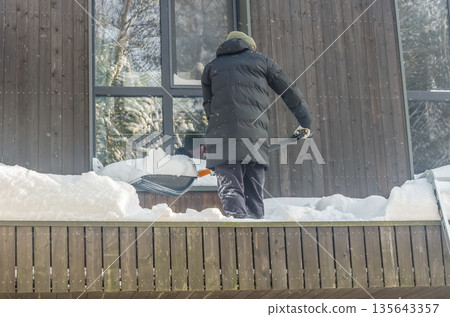 Man Shoveling Deep Snow From a Modern House Balcony. Man Shoveling Deep Snow From a Modern House Balcony. 135643357