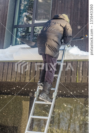 Risky Winter Chore: Man Climbing Ladder to Shovel Roof Snow. 135643360