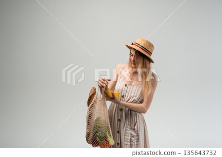Young woman selecting bananas from reusable mesh grocery bag, zero waste shopping and healthy lifestyle concept with copy space 135643732