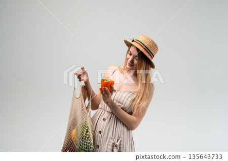 Young woman choosing fresh vegetables from reusable mesh bag, healthy eating and sustainable shopping concept 135643733