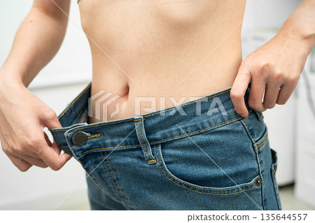 Young Asian woman losing weight wearing loose pants in oversize jeans. Young Asian woman losing weight wearing loose pants in oversize jeans. 135644557