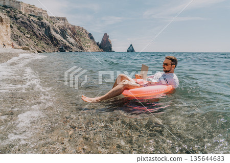 Freelancer beach remote man working on laptop while floating in the sea on inflatable ring during summer vacation Freelancer beach remote man working on laptop while floating in the sea on inflatable ring during summer vacation 135644683