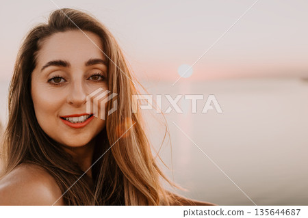 Woman sunset portrait featuring a smiling young lady at the beach during golden hour with warm sunlight and sea background Woman sunset portrait featuring a smiling young lady at the beach during golden hour with warm sunlight and sea background 135644687