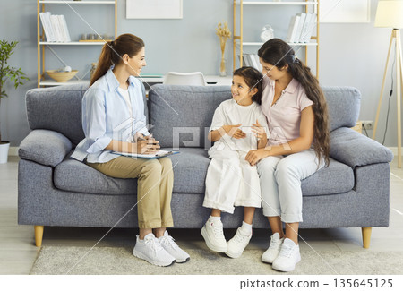 Psychologist counsels mother and child at home for family therapy session on sofa 135645125
