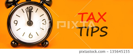Tax tips symbol. Concept word Tax tips on beautiful orange paper. Beautiful black alarm clock. Beautiful orange paper background. Business tax tips concept. Copy space. Tax tips symbol. Concept word Tax tips on beautiful orange paper. Beautiful black alarm clock. Beautiful orange paper background. Business tax tips concept. Copy space. 135645155