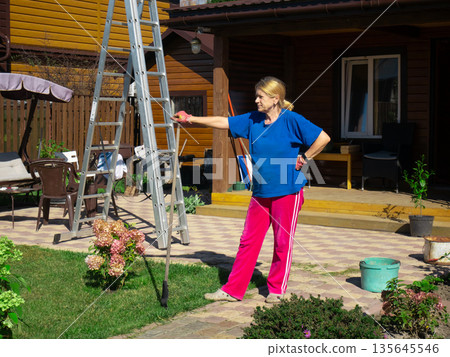 Mature woman outdoor with ladder. Senior woman doing home repair work on house. Renovation or DIY concept. Housewife at home. 135645546