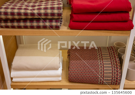 Folded textiles on shelves: red, plaid, white, and patterned fabrics 135645600
