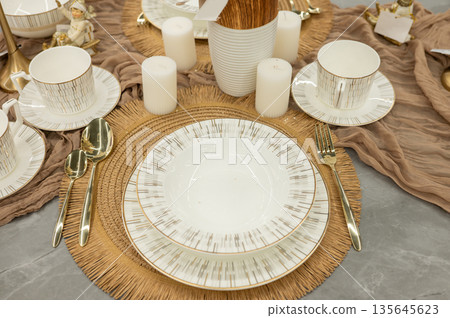 Elegant table setting with white ceramics and gold cutlery on woven placemat 135645623