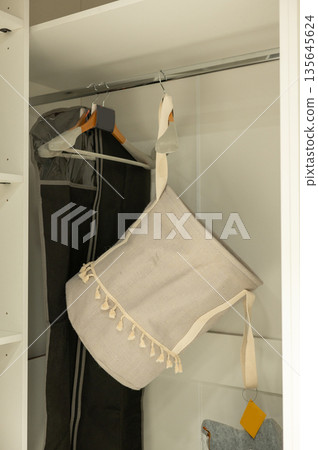 Closet storage with beige hanging laundry bag and clothes hangers Closet storage with beige hanging laundry bag and clothes hangers 135645624