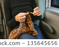Young caucasian female knitting in cozy setting with yellow crochet hook 135645656
