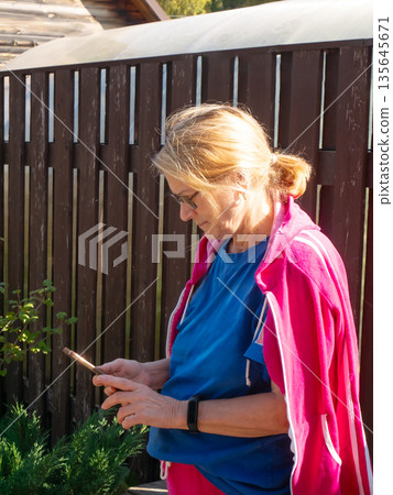 Woman using smartphone outdoor in rural setting with wooden fence, digital communication and technology concept for everyday life 135645671