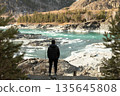Man Observing Icy Turquoise River in Winter Mountain Landscape 135645808