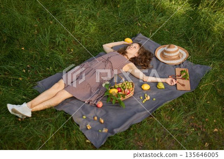 Serene young woman lounging outdoors during golden evening light Serene young woman lounging outdoors during golden evening light 135646005