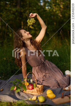 Woman daydreaming with grapes on blanket outdoors 135646039