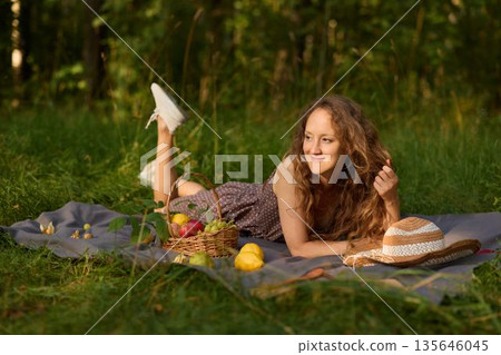Serene woman reclines on blanket amid trees with fruit nearby Serene woman reclines on blanket amid trees with fruit nearby 135646045
