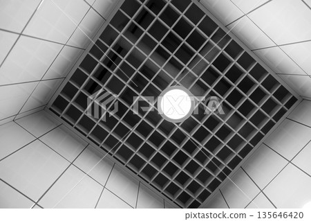 A monochrome interior shot of a tiled ceiling with a light 135646420