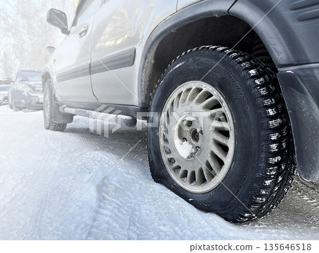Deflated car wheel. Car is in parking lot. A broken wheel at the car in the cold, in winter. Close up photo 135646518