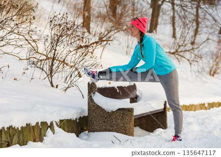 Girl stretching on bench in winter Girl stretching on bench in winter 135647117