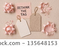 Rethink tag message with pink paper flower, piggy bank, notebook, and scattered origami decorations on neutral background representing sustainable gift wrapping concept 135648153