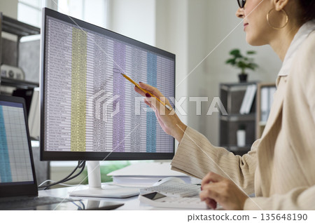 Businesswoman reviewing spreadsheet data on monitor during financial audit in office 135648190