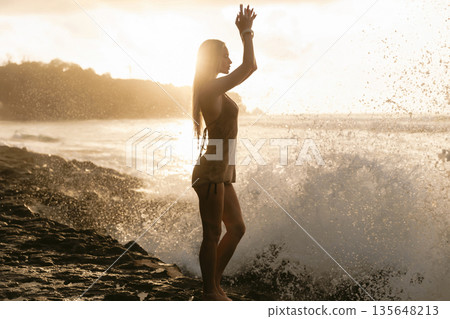 Silhouette of slim woman on rocky beach at sunset with ocean waves, natural beauty concept Silhouette of slim woman on rocky beach at sunset with ocean waves, natural beauty concept 135648213