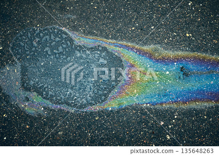Vivid oil spill crafts an eye-catching iridescent pattern on the damp pavement. Vivid oil spill crafts an eye-catching iridescent pattern on the damp pavement. 135648263
