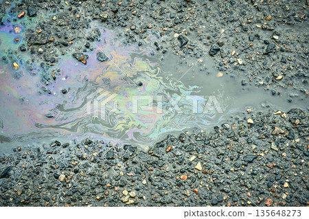 Oil slick creating a colorful rainbow pattern in a puddle on rough asphalt. 135648273