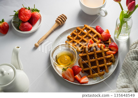 Belgian waffles with strawberries and honey, cup of tea and fresh fruits. Homemade breakfast table setting with tulip flower bouquet 135648549