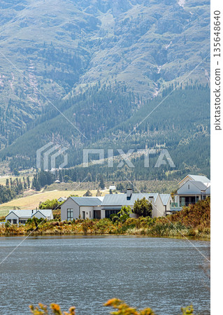 Scenic view of homes near a tranquil lake with lush mountains in the background Scenic view of homes near a tranquil lake with lush mountains in the background 135648640