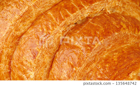 Extreme close up of crispy croissant texture. Macro shot of golden brown flaky puff pastry surface. Extreme close up of crispy croissant texture. Macro shot of golden brown flaky puff pastry surface. 135648742