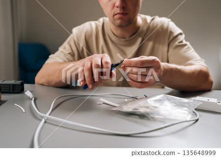 Cropped shot of repairman working with electronic components, stripping insulation from cable repairing, assembling wiring, demonstrating hobby electronics project or household electrical maintenance. Cropped shot of repairman working with electronic components, stripping insulation from cable repairing, assembling wiring, demonstrating hobby electronics project or household electrical maintenance. 135648999