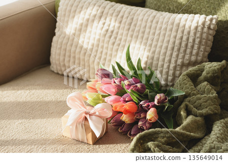 Tulip Bouquet and Gift Box on Cozy Sofa. Warm Spring Flatlay with Soft Textures Tulip Bouquet and Gift Box on Cozy Sofa. Warm Spring Flatlay with Soft Textures 135649014