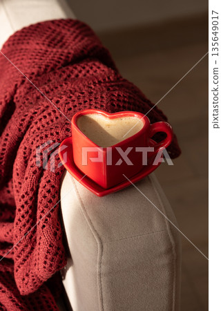 Heart Shaped Coffee Cup on Armchair with Red Blanket. Cozy Valentines Day Still Life Heart Shaped Coffee Cup on Armchair with Red Blanket. Cozy Valentines Day Still Life 135649017