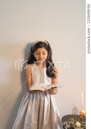 A young girl is reading a book while wearing a silver dress 135649036