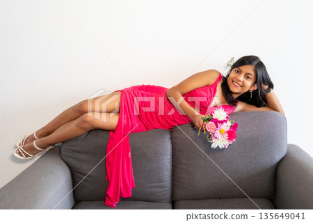 A teen in a pink dress is laying on a couch with a bouquet of flowers in A teen in a pink dress is laying on a couch with a bouquet of flowers in 135649041