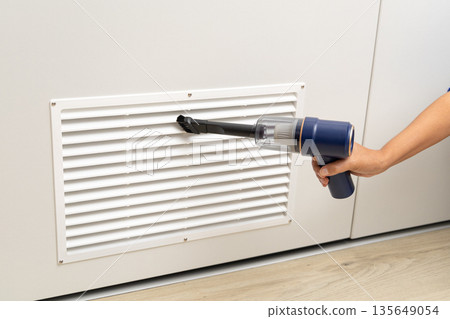 A person is using a vacuum cleaner to clean a vent A person is using a vacuum cleaner to clean a vent 135649054