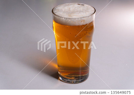 Full pint glass of golden lager beer with frothy foam head. Vertical studio shot of amber ale on white background with copy space 135649075