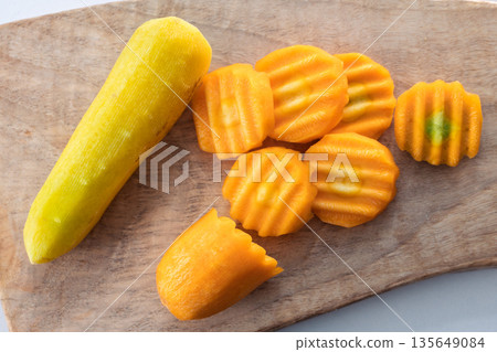 Peeled yellow carrot with crinkle cut slices on a wooden board. Fresh raw vegetable preparation top view Peeled yellow carrot with crinkle cut slices on a wooden board. Fresh raw vegetable preparation top view 135649084