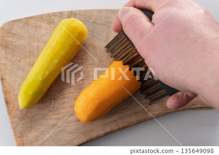 Hand slicing fresh orange carrot with crinkle cut knife on wooden board. Preparation of raw yellow and orange vegetables for healthy meal 135649098