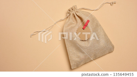 A rough canvas bag with drawstrings, decorated with a craft tag and a red clothespin. Beige background. 135649455