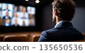 Man in business suit attending virtual conference watching multiple participants on large screen in dark room 135650536