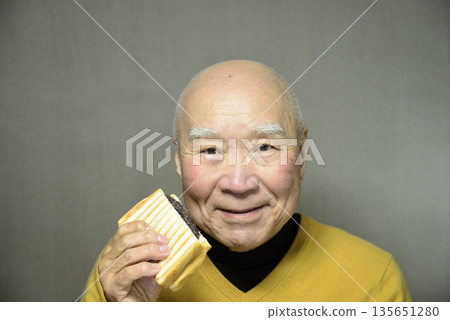 一位老人家正在吃熱騰騰的豆醬三明治。 135651280