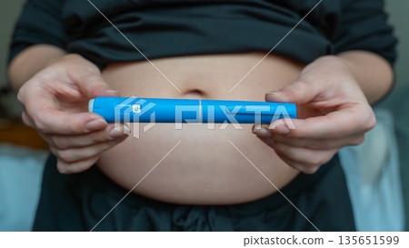 GLP-1 injection pen held by woman in front of abdomen, weight management concept GLP-1 injection pen held by woman in front of abdomen, weight management concept 135651599