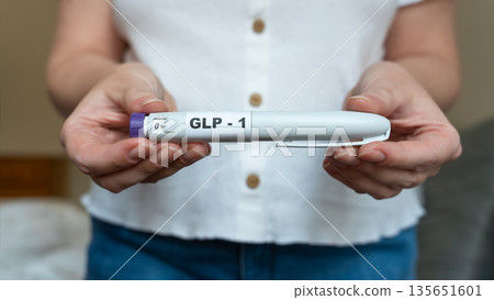 GLP-1 injection pen held by woman in front of abdomen, weight management concept GLP-1 injection pen held by woman in front of abdomen, weight management concept 135651601